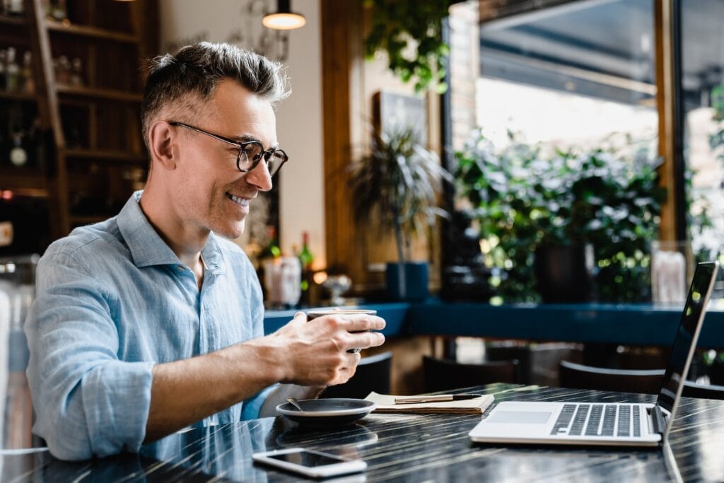 Boss enjoying breakfast coffee in restaurant working remotely on laptop watching webinars online